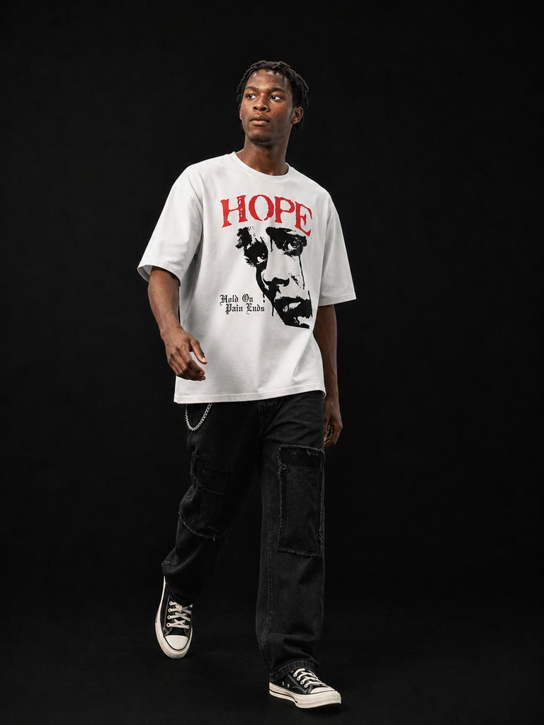A man modeling a white graphic t-shirt featuring a black portrait of John Gotti and the word 'HOPE' in red, paired with black cargo pants and black sneakers, set against a solid black studio background.